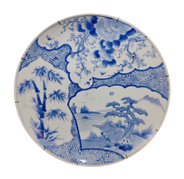 A 19th century Japanes arita blue and white large dish painted with panels of landscape bamboo and plum blossom